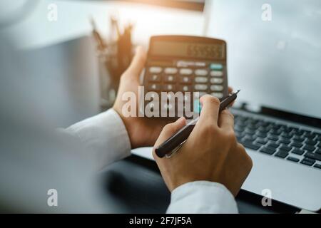 Geschäftsmann Buchhalter mit Taschenrechner. Gestresster junger Mann, der Kontostand, Rechnungen, Steuern und die Berechnung der Ausgaben im Home Office überprüft. Stockfoto