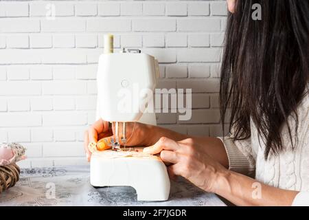 Schöne Brünette junge Frau näht Kleid mit der Nähmaschine. Nähen zu Hause als Hobby. Selective Focus Maschine und Hände. Stockfoto