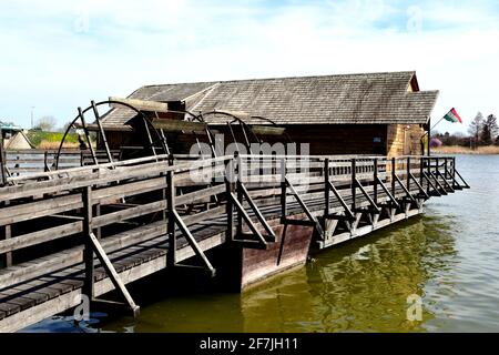 Historische hölzerne schwimmende Bootsmühle. Grünes Flusswasser. Große Boothaus-ähnliche Struktur mit riesigen Spinning Mill Räder Holzplankenblätter. Blauer Himmel Stockfoto