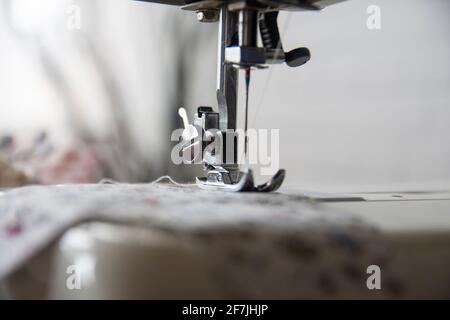 Nähmaschinenbedienung aus verschiedenen Blickwinkeln und Nähen eines geblümten Stoffes. Selektiver Fokus Maschinenteil. Stockfoto