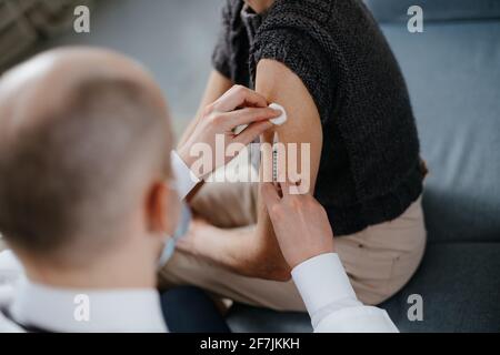 Der erfahrene Arzt in einer Maske impft in seinem Büro. Stockfoto