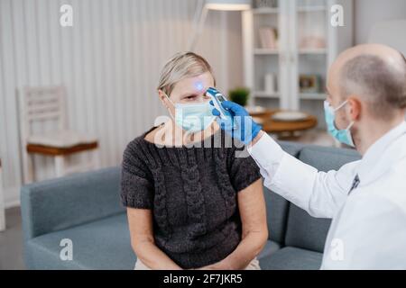 Hausarzt, der die Temperatur einer reifen Frau misst. Stockfoto