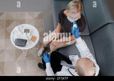 Der Arzt misst die Temperatur einer Frau während eines Hausbesuches. Stockfoto