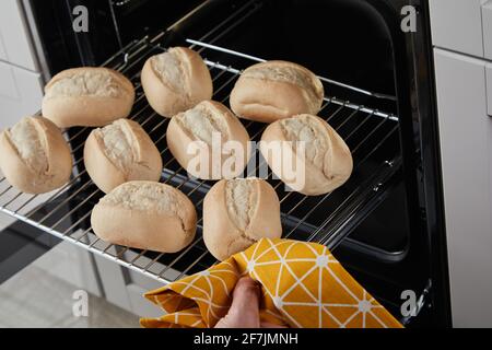 Von oben gesichtslose Person mit Handtuch entfernen heißen Glide Rack Mit frischen Brötchen aus dem Ofen Stockfoto