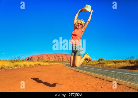 Fröhliche Touristenfrau mit Hut springt am Uluru Ayers Rock im Uluru-Kata Tjuta National Park. Lifestyle-Reisende genießen im australischen Outback Red Stockfoto