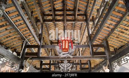 Rote Laterne, die in einem Holzträger eines alten Hauses hängt. Stockfoto