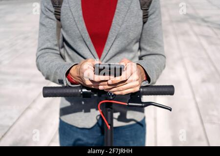 Stock Foto von einem Geschäftsmann in Jacke mit Rucksack Stehen auf Elektroroller und mit Smartphone Stockfoto