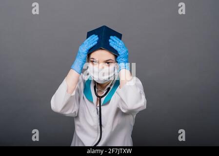Schöne Ärztin in Schutzmaske wegschauen und über etwas nachdenken. Stockfoto