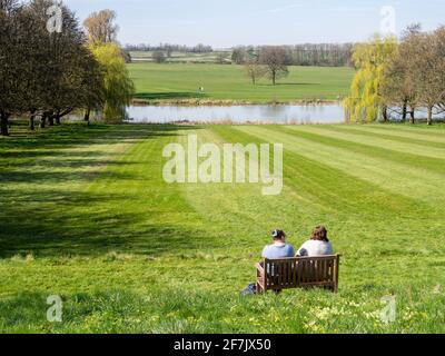 Zwei Damen, die auf einer Bank sitzen und den Blick auf den See genießen, Kelmarsh Hall, Northamptonshire, Großbritannien. Stockfoto