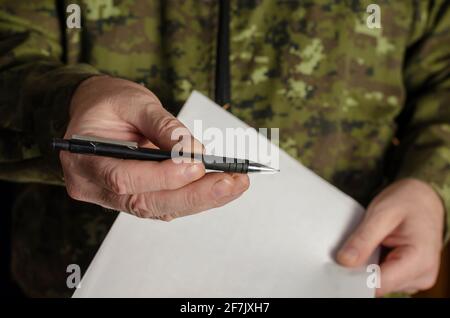 Ein Offizier hält einen schwarzen Stift an die Kamera. Eine Männerhand bietet einen Stift an, um ein Dokument zu unterschreiben. Mann mittleren Alters. Selektiver Fokus. Low-Taste. In Innenräumen Stockfoto