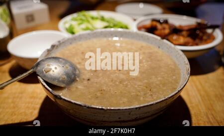 Eine Schüssel Reispaste, auch Porridge genannt, in einer Schüssel mit anderen Gerichten auf dem Tisch. Stockfoto