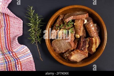 Konservierte Schweinefleischrippen, Lende und Schweinewurst in einem Tontopf mit einem Rosmarinzweig auf schwarzem Hintergrund, typisch spanische Küche Stockfoto