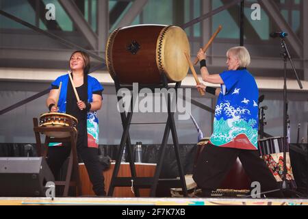 Frauen spielen Taiko oder traditionelle japanische Holztrommeln. Die größere Trommel ist eine chu-daiko und die kleinere eine shimi-daiko Stockfoto