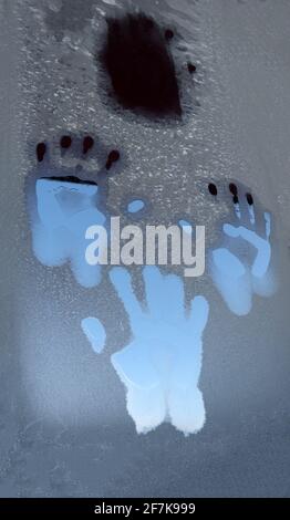 Spuren der Handflächen auf dem mit Frost bedeckten Glas. Stockfoto