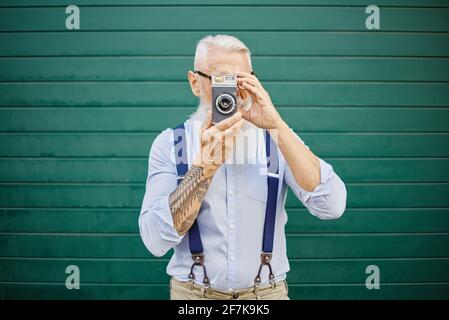 Fröhlicher Flusspferde mit alter Vintage-Kamera an der roten Wand - reifer, stilvoller Fotograf, der Spaß hat, die Welt zu bereisen - fröhliches älteres Lifestyl Stockfoto
