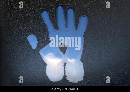 Spur der Handfläche auf dem mit Frost bedeckten Glas. Die Handfläche schmolz das Eis auf dem Glas. Stockfoto