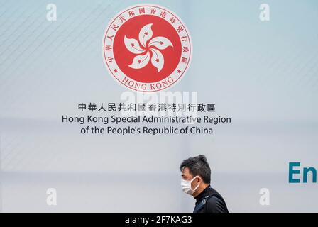 Hongkong, China. April 2021. Ein Fußgänger mit Gesichtsmaske geht an Hongkongs Emblem auf einem Regierungsbanner vorbei, das das Wahlsystem fördert. (Foto von Miguel Candela/SOPA Images/Sipa USA) Quelle: SIPA USA/Alamy Live News Stockfoto