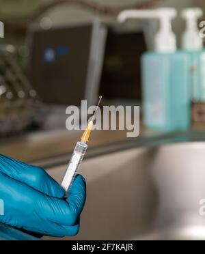 Vorbereitung der Spritze für die Impfung, Arzthand in Gummihandschuhen, Nahaufnahme. Desinfektionsmittel im Hintergrund. Stockfoto