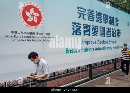 Hongkong, China. April 2021. Menschen mit Gesichtsmasken kommen an einem Transparent der Regierung vorbei, das an einem Zaun auf dem Spielplatz hängt und auf dem steht: „Verbessere das Wahlsystem, Sorge dafür, dass Patrioten Hongkong verwalten“. (Foto von Miguel Candela/SOPA Images/Sipa USA) Quelle: SIPA USA/Alamy Live News Stockfoto