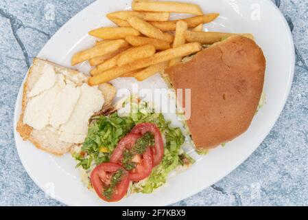 Blick von oben auf das große Churrasquito-Sandwich liegt offen mit saftigen Tomatenscheiben auf der Oberseite serviert mit pommes frites. Stockfoto