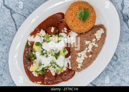 Blick von oben auf Hühnerchiladas in roter Sauce, serviert mit gebratenen Bohnen und Reis für ein leckeres mexikanisches Essen. Stockfoto