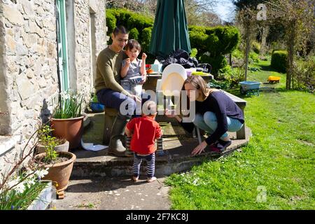 Eltern Mutter Vater Kinder junge Familie sitzt außerhalb Haus Urlaub Ferienhaus am sonnigen Osterwochenende in einem Garten in West WALES UK KATHY DEWITT Stockfoto