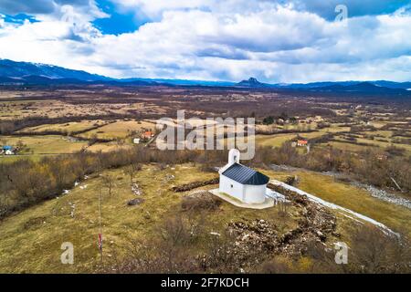 Lika-Region. Kirche auf dem Hügel in Lovinac und Velebit Berg in Lika Landschaft Luftbild. Ländliches Kroatien Stockfoto