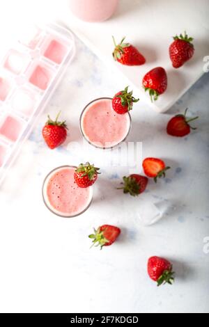 Frischer hausgemachter kalter Erdbeer-Smoothie mit Eiswürfeln und frischen Erdbeeren auf weißem Hintergrund. Draufsicht. Stockfoto