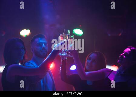 Junge Freunde tanzen mit Gläser Champagner in der Hand. Gegen Beleuchtung Geräte als Hintergrund. Freunde der jungen Menschen tanzen. Stockfoto