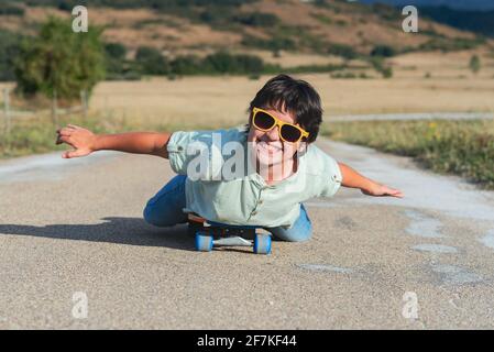 Fröhliches Kind mit Skateboard und Sonnenbrille auf der Straße im Freien Stockfoto