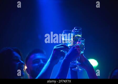 Junge Freunde tanzen mit Gläser Champagner in der Hand. Gegen Beleuchtung Geräte als Hintergrund. Freunde der jungen Menschen tanzen. Stockfoto