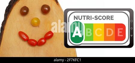 Nutri-Score-Logo auf einem Handy-Display neben einem lachenden Gesicht aus Tomaten auf einem Holzbrett. Nutri-Score ist ein Nährwertkennzeichnungssystem für Stockfoto