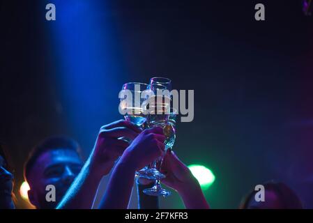 Junge Freunde tanzen mit einem Glas Champagner in den Händen. Gegen Beleuchtungseinrichtungen als Hintergrund. Junge Freunde tanzen. Stockfoto