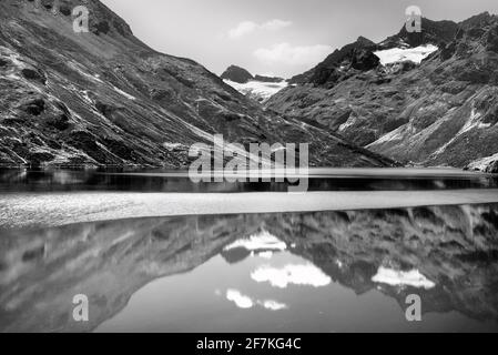 Malerische Alpenlandschaft mit See, Bergen und Gletscher. Reflexionen in einem ruhigen Bergsee. Schwarzweiß-, Schwarzweiß- und Schwarzweißfotografie. Stockfoto
