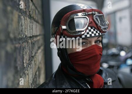 Schöne weibliche Biker, Cafe Racer mit Schal Mund Abdeckung Motorradhelm und Brille in London, Großbritannien Stockfoto