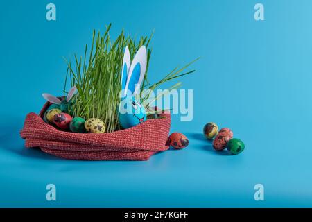 Blaues Ei mit Hasenohren und ostereiern im Gras Stockfoto