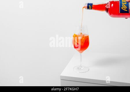 Lugansk, Ukraine - 29. März 2021: Aperol Spritz Cocktail. Gießen aperol in Weinglas mit Eis auf weißem Hintergrund. Langes kohlensäurehaltiges Getränk. Minimale Kreati Stockfoto