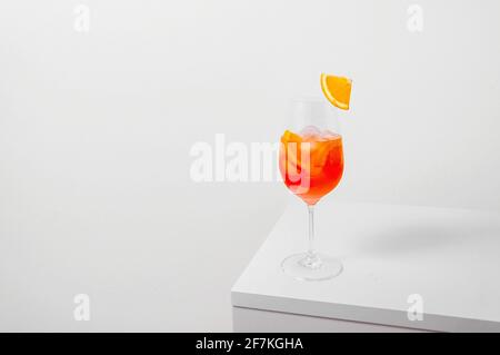 Aperol Spritz Cocktail in Weinglas mit Eis und Orangenscheibe auf weißem Hintergrund. Langes kohlensäurehaltiges Getränk. Minimales kreatives Konzept. Stockfoto