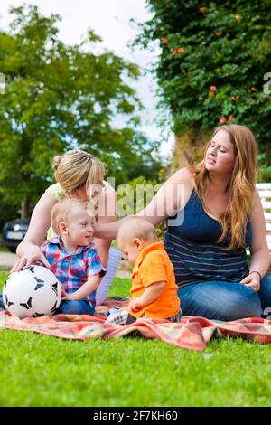 Glückliche junge Mutter und Großmutter sitzen mit ihren Kindern und Enkelkinder in einem Park im Freien auf einer Bank Stockfoto