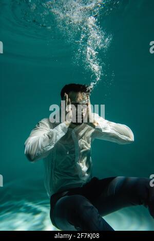 Arabischer Geschäftsmann mit Händen in der Nähe des Kopfes, der im Pool unter Wasser schwimmend ist Stockfoto