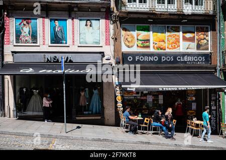 Porto, Portugal. April 2021. In einer der belebtesten Straßen von Porto ist die Aktivität langsam, da nur zwei Personen auf der Promenade sitzen sehen. Die zweite Phase des Definationsprozesses in Portugal begann am 5. April. Restaurants und Cafés durften Menschen auf den Tischen im Freien in Gruppen von 4 Personen pro Tisch beherbergen und die Menschen können nun mit mehr Freiheit durch die Stadt gehen. Kredit: SOPA Images Limited/Alamy Live Nachrichten Stockfoto