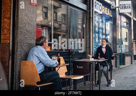 Porto, Portugal. April 2021. Zwei Freunde sitzen an verschiedenen Tischen auf einer Terrasse eines Restaurants und führen ein Gespräch, das den Anweisungen der Regierung zur sozialen Distanzierung folgt. Die zweite Phase des Definationsprozesses in Portugal begann am 5. April. Restaurants und Cafés durften Menschen auf den Tischen im Freien in Gruppen von 4 Personen pro Tisch beherbergen und die Menschen können nun mit mehr Freiheit durch die Stadt gehen. Kredit: SOPA Images Limited/Alamy Live Nachrichten Stockfoto