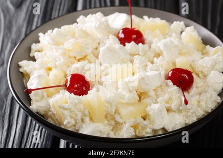 Süßer Salat aus Reis, Salatmarmelibe und Ananas mit Schlagsahne in Nahaufnahme auf einem Teller auf dem Tisch. Horizontal Stockfoto