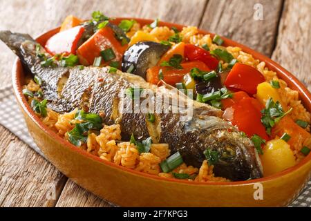 Thieboudienne, traditionelles westafrikanisches Fisch- und Reisgericht mit Gemüse in der Schale auf dem Tisch. Horizontal Stockfoto