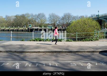 Eine Joggerin nähert sich der richmond-Schleuse und dem Wehr neben einer Straße, die mit Parkgenehmigungsdetails gekennzeichnet ist, auf der twickenham-Seite der themse, london Stockfoto