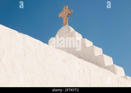 Nahaufnahme eines weißen Daches, das Äußere einer Kirche mit einem Steinkreuz, Griechenland, Kykladen-Inseln, Mykonos. Blauer Himmel im Hintergrund. Konzeptreise Stockfoto