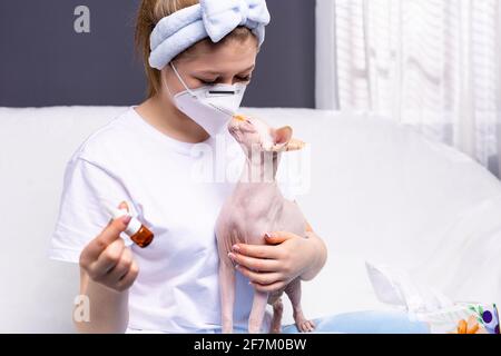 Eine Frau in einer Schutzmaske mit Tropfen zu Hause während der Quarantäne. Schutz anderer vor der Ausbreitung des Virus. Die Sphinx will die küssen Stockfoto