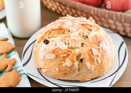 Frisch gebackener, hausgemachter Süßkuchen mit Mandeln und Rosinen auf Holztisch. Osterkaib. Korb mit Birnen und Äpfeln. Vintage Flasche Milch. Grün Stockfoto