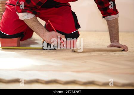 Baumeister Mann für die Installation des Holzbodens in der Renovierung eines Hauses. Zimmermann verlegt Laminatboden im Raum Stockfoto
