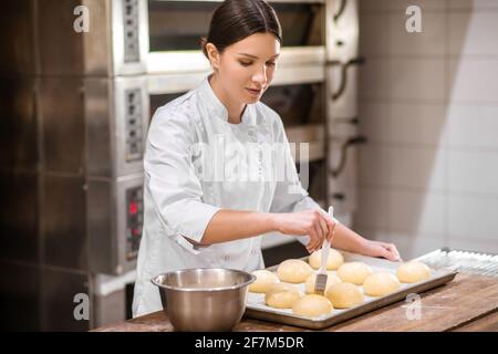 Frau, die vor dem Backen Glasuren auf Brötchen aufgibt Stockfoto